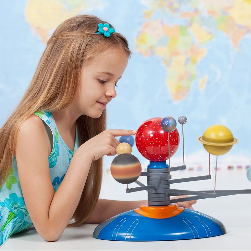 Little girl studies the solar system in geography class - looking at the scale model of planets